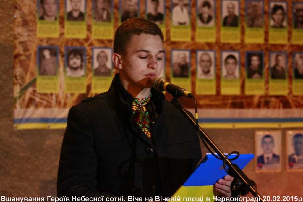 Юнак у вишиванці читає промову біля мікрофона на тлі портретів 
Героїв Небесної Сотні