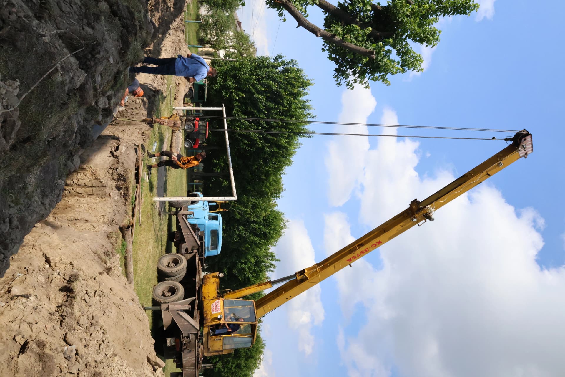 кран опускає нову водопровідну трубу у траншею