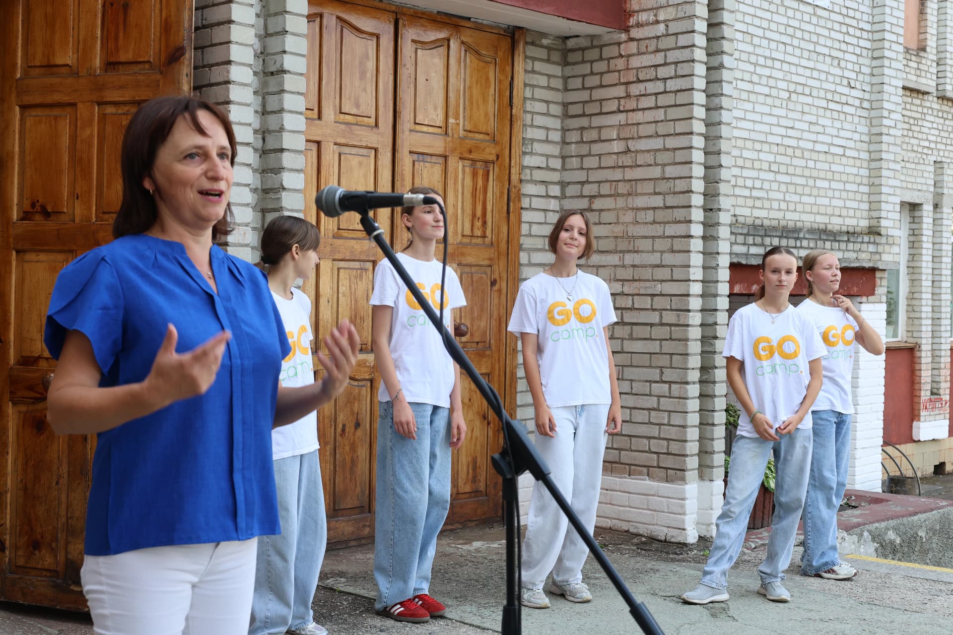 вичтель стоїть перед мікрофоном, а поряд четверо дівчат