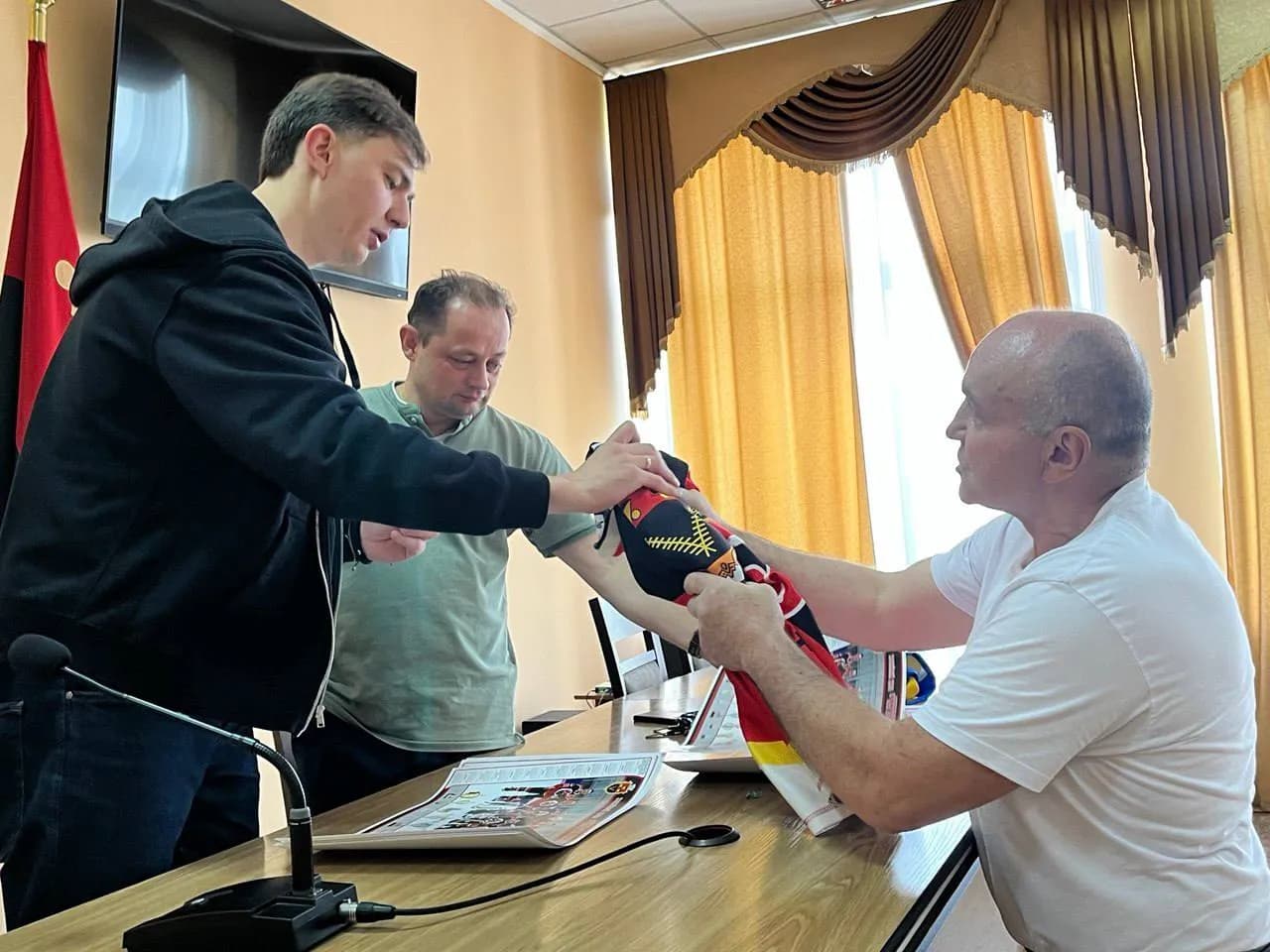 президент хокейного клубу передає хокеїсту хокейну футболку свого клубу