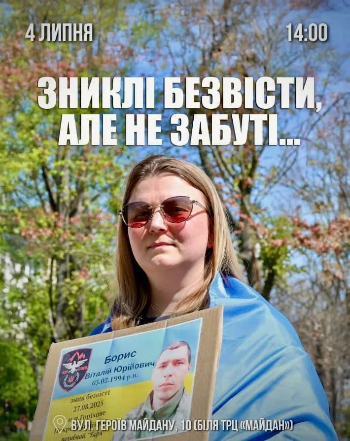 На фото жінка в сонцезахисних окулярах, на плечах якої накинуто синьо-жовтий прапор. Вона тримає в руках портрет зниклого безвісти захисника України Бориса Віталія Юрійовича.