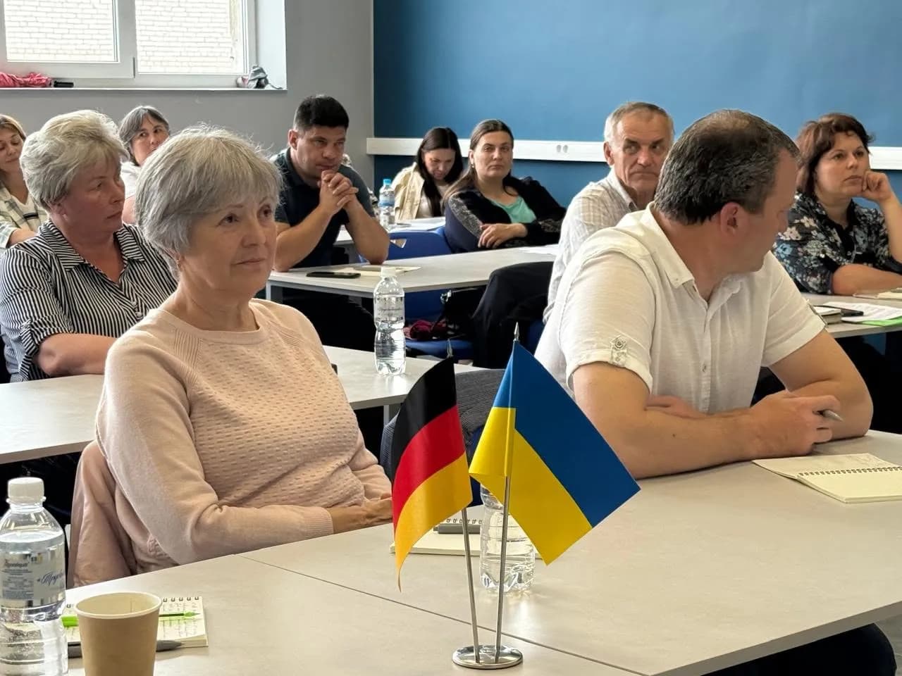 В аудиторії дорослі люди сидять за партами і слухають лекцію