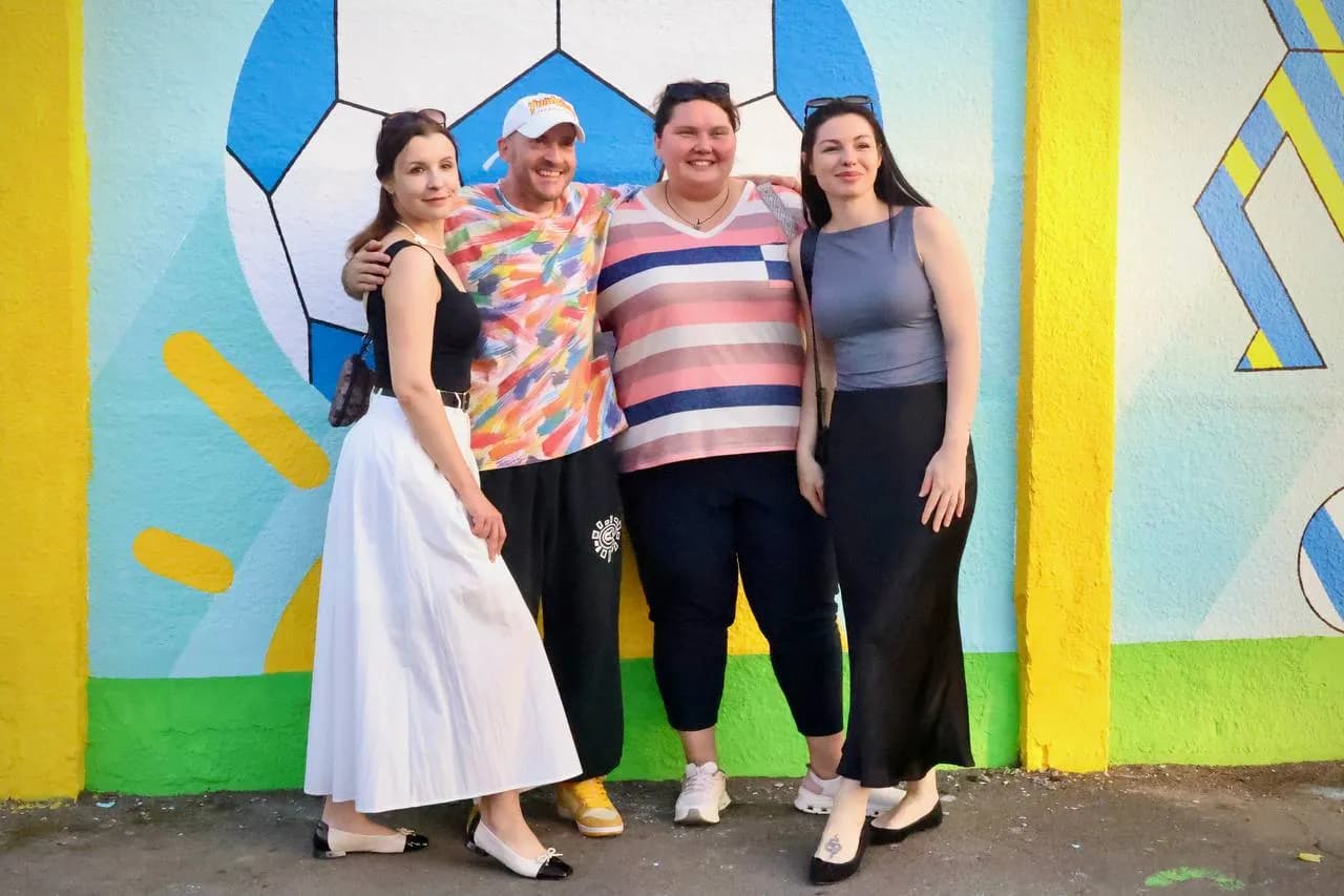 Гості фестивалю фотографуються з художником на фоні муралу