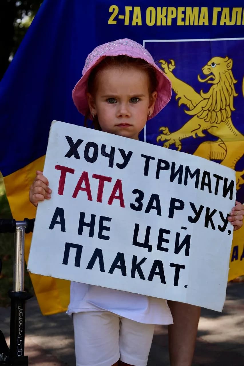 Маленька дівчинка тримає плакат з написом "Хочу тримати тата за руку, а не цей плакат"